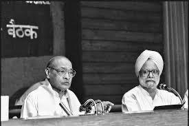 In this photo, Rao and Singh are sitting together at a long table with microphones in front of them. Rao is looking straight ahead with a serious expression, and Singh is sitting next to him. This looks like a press conference where they are explaining the new economic changes to the public.