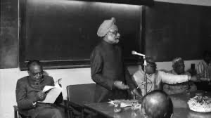 This photo shows Manmohan Singh standing up at a table to give a speech. He is gesturing with his hands while Prime Minister Rao sits to the left, reading through a book or a report. This captures the moment Singh was presenting the new ideas that would change India's future.