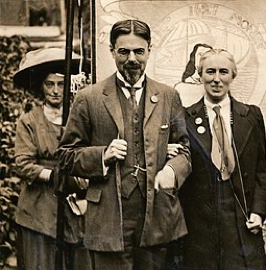 Laurence and Clemence Housman wearing Suffrage Badges and standing in front of a Suffrage Banner, circa 1911. LSE Library. Wikimedia Commons.