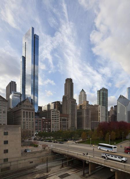 Photo of E Monroe Drive in Chicago, Illinois. A view of Chicago's sky, buildings, and street. There is a large, bright skyscraper to the left, towering above the surrounding buildings and street. 