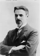 Photographed half portrait of Laurence Housman turned slightly to his left with crossed arms, wearing a suit, tie, and pocket square