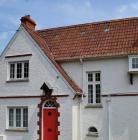 Close-up photo of white 1920s house with red door and steep red tiled roof
