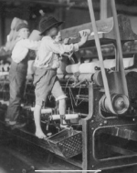 Two boys working at a mill. They look to be around the age of 6 to 7. Both are stepping on the actual machine due to being too short to operate it normally. 