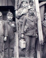 A black and white image of six young boys covered in dust and dirt. Somber expressions cover their faces. Outfits resemble those of chimney sweeps.