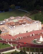 An aerial view of the front facade of Buckingham Palace and the surrounding red entrance lanes, fountains, etc.