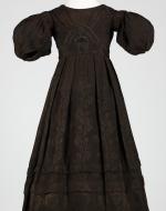 Small Victorian girl's dress in brown with puffed sleeves and pleated skirt.