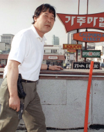This image depicts a Korean man defending his store from a rooftop in Los Angeles. Furthermore, he is armed with a handgun (Lah).