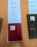 A small red book sitting on a blue slip of paper labeled: "Item Number 48, Creation date 1925-1930, Edition available digitally? NO"
