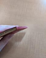 A hand holds the book, with the camera pointed down the spine of the book, demonstrating the way the spine has a slight twist to it.