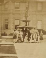 Photograph of a group portrait of Queen Victoria and Prince Albert with their seven eldest children and Queen Victoria's mother, the Duchess of Kent. The group are posed in front of a fountain at Osborne House. The group stand, positioned from left to right are: Albert Edward, Prince of Wales, Princess Victoria, Princess Royal, Prince Arthur, Princess Alice, Prince Albert, Queen Victoria, Princess Louise, the Duchess of Kent, Princess Helena and Prince Alfred.
