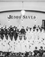 The meeting of the KKK with a sign in the background that reads "Jesus Saves"