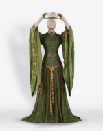 A long green dress, with large sleeves and a gold belt. The dress, a Lady Macbeth costume made with beetles’ wings, is on a mannequin that is holding a crown above its head.