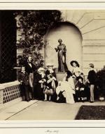 Photograph of a group portrait of Queen Victoria and Prince Albert with their family taken in the grounds of Osborne House. The photograph depicts, from left to right, Prince Alfred, Prince Albert, Princess Helena, Princess Alice, Prince Arthur, Queen Victoria holding Princess Beatrice in her arms, Princess Victoria, Prince Leopold and Prince Albert Edward of Wales. The family pose in front of a sculpture of a full length female figure, positioned in in an alcove.