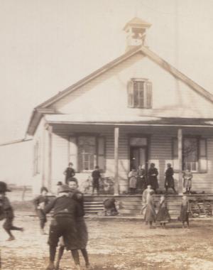 This is a photo of Amish children playing in front of a one-room schoolhouse