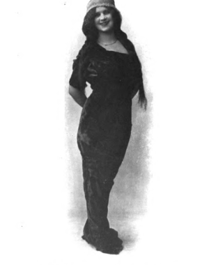 a full-body portrait of Lydia Taylor wearing a long dress and hat