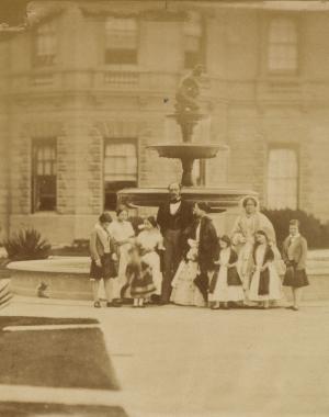 Photograph of a group portrait of Queen Victoria and Prince Albert with their seven eldest children and Queen Victoria's mother, the Duchess of Kent. The group are posed in front of a fountain at Osborne House. The group stand, positioned from left to right are: Albert Edward, Prince of Wales, Princess Victoria, Princess Royal, Prince Arthur, Princess Alice, Prince Albert, Queen Victoria, Princess Louise, the Duchess of Kent, Princess Helena and Prince Alfred.