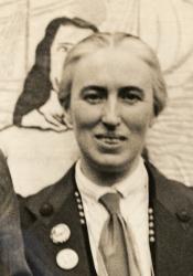 Cropped newspaper photo of Clemence Housman wearing suffrage buttons and standing in front of a suffrage banner