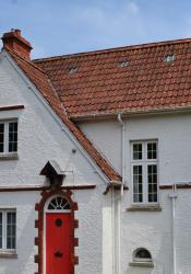 Close-up photo of white 1920s house with red door and steep red tiled roof