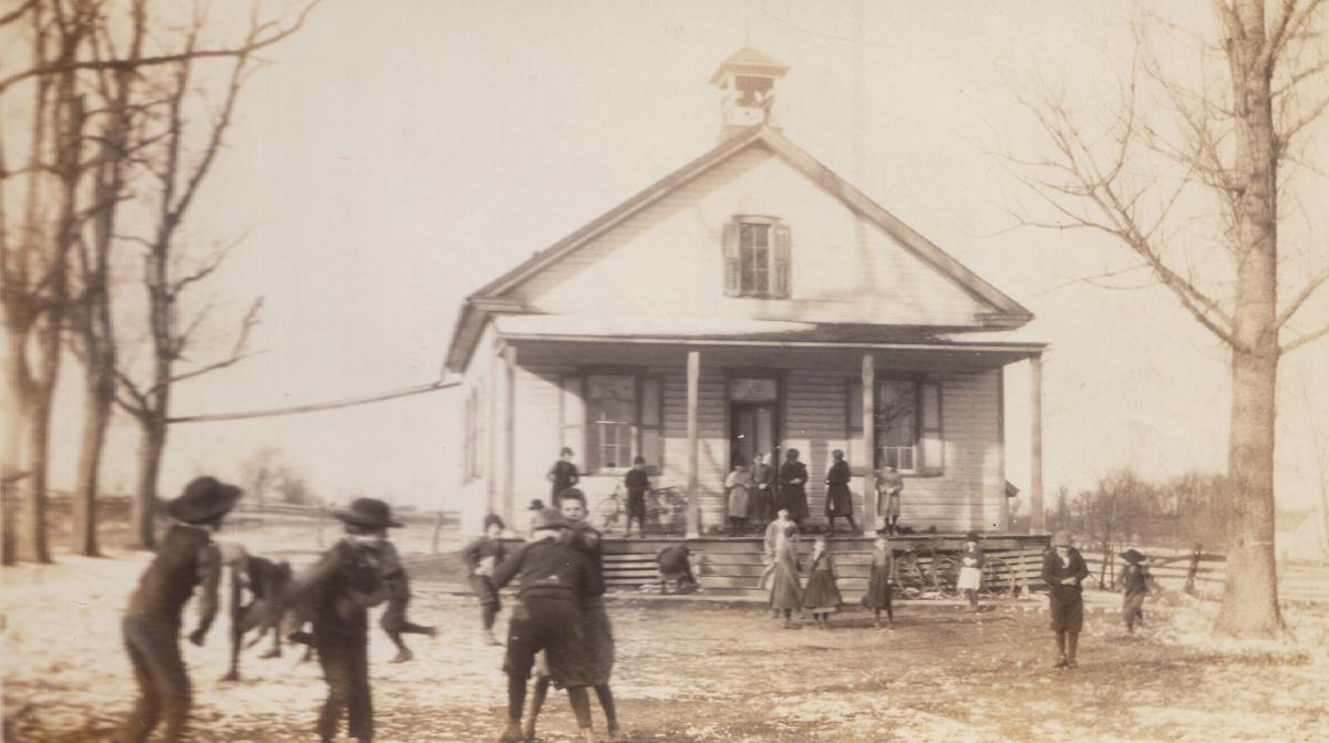 This is a photo of Amish children playing in front of a one-room schoolhouse