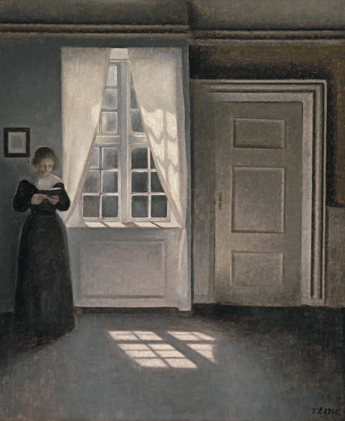 A woman is reading a book next to a window where the sunlight passes through showing the window's shadow.